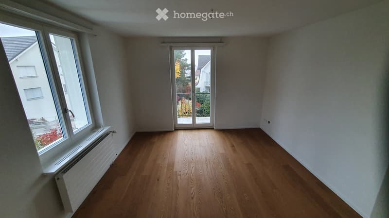 Empty room with wooden flooring, large windows, and a sliding glass door leading to a balcony or outdoor area.