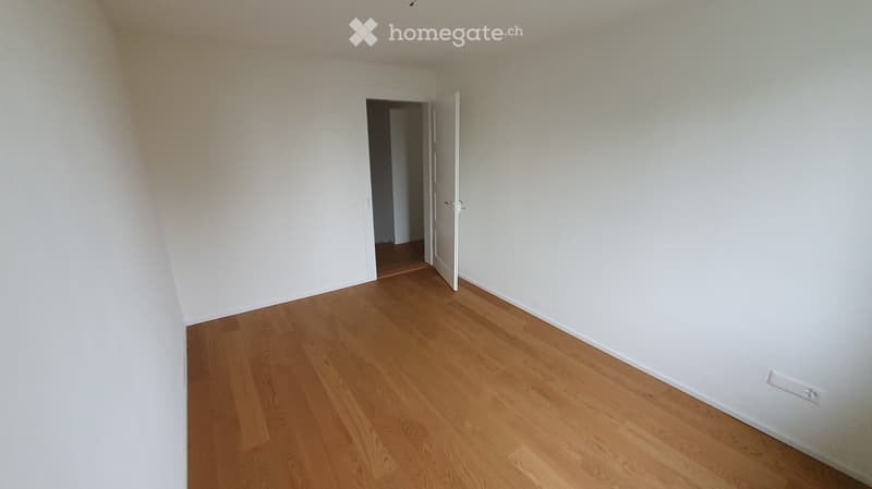 Empty room with light wooden flooring and white walls, featuring an open doorway leading to another space.