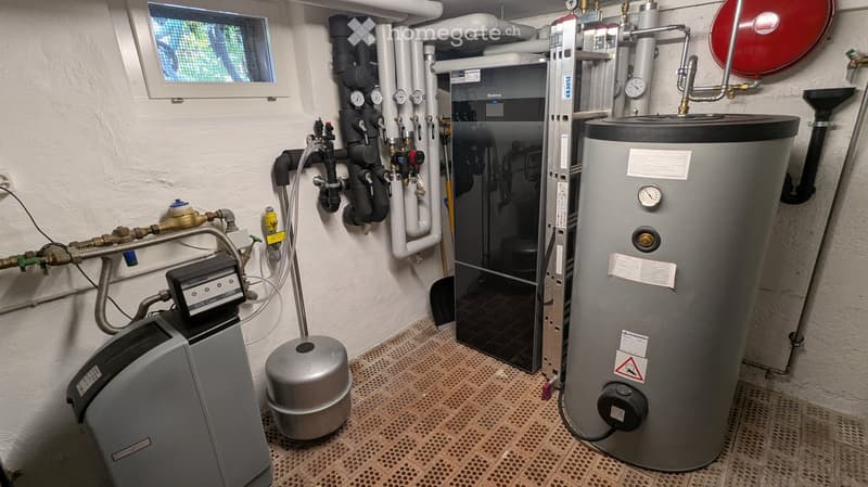 Modern bathroom utility area with water heater, control panel, pipes, valves, gauges, and a small window.