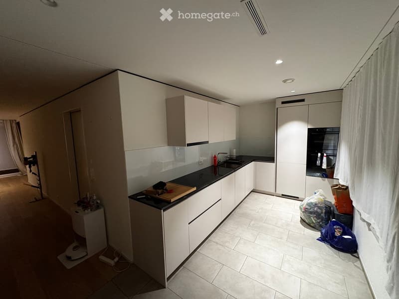 Modern kitchen with white cabinets, black countertop, and stainless steel appliances. Visible items include a sink, faucet, oven, and cutting board.