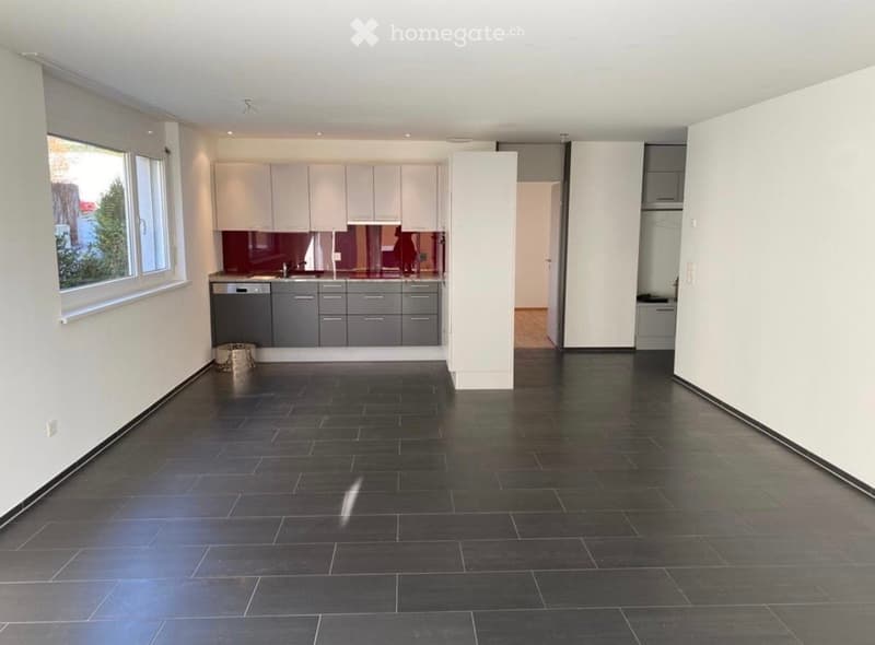 Modern kitchen with white cabinets, dark grey lower cabinets, and a dark tiled floor. Features a large window with a view of greenery outside.