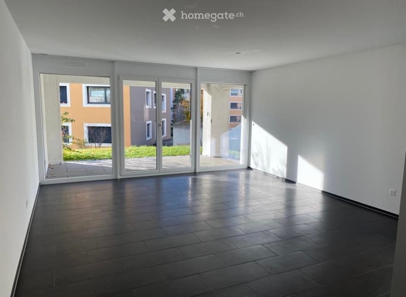 Empty room with dark tiled floor, white walls, and large sliding glass doors leading to an outdoor area.
