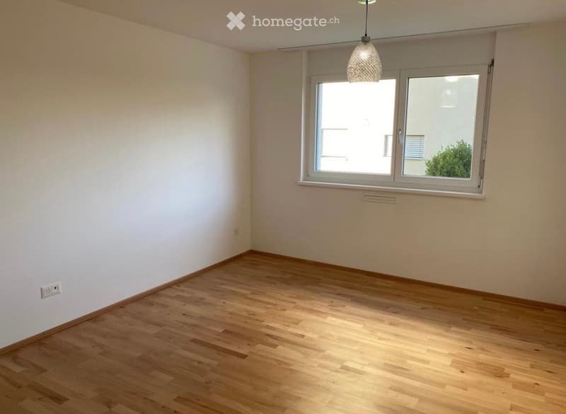 Empty room with wooden flooring, white walls, and a large window with a view of the outside.