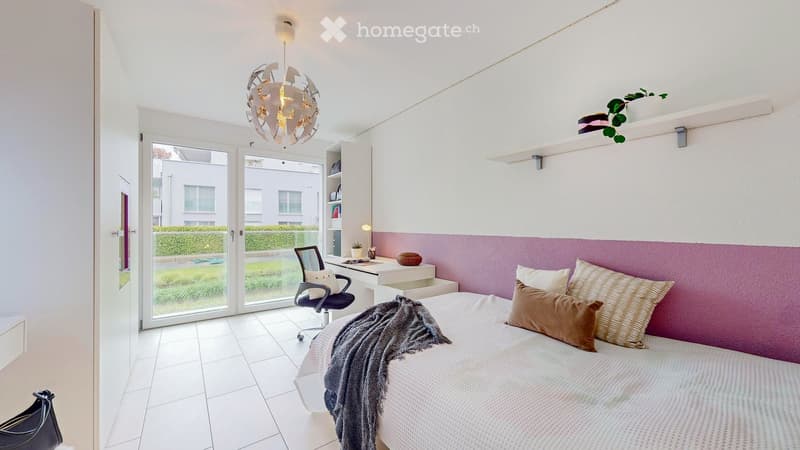 Modern bedroom with white walls, pink accent wall, large bed with pillows and blanket, desk with chair, and a hanging light fixture.