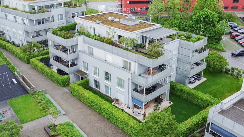 Modern multi-story residential building with balconies, rooftop garden, and surrounding greenery.