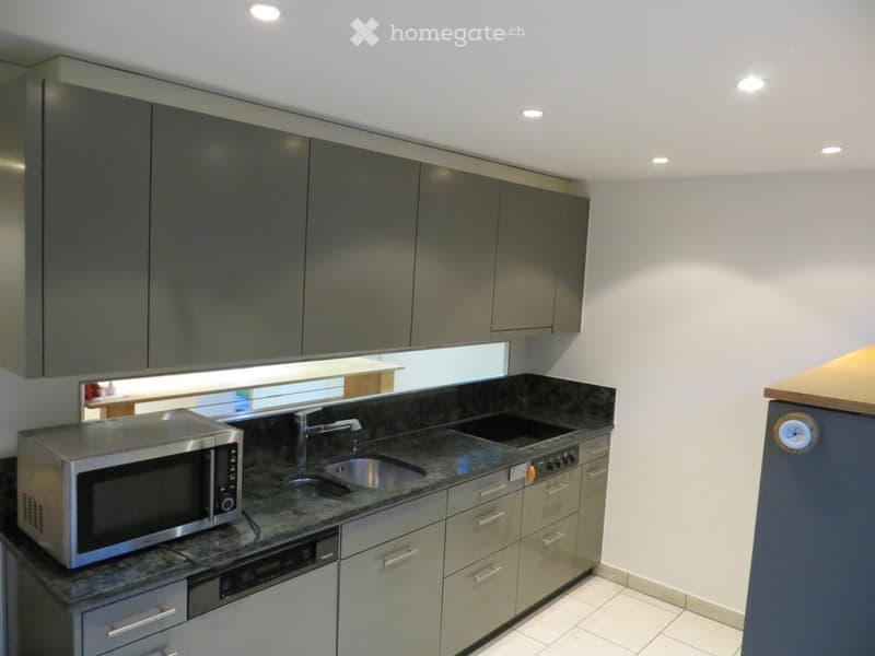 Modern kitchen with grey cabinets, granite countertop, stainless steel sink, microwave, and dishwasher.