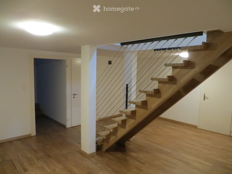 Modern hallway with wooden flooring, a staircase with wooden steps and a glass railing, and white walls.