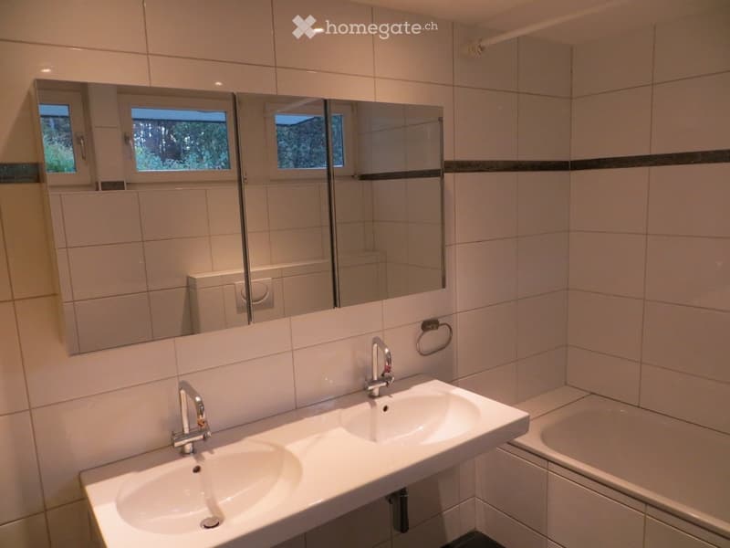 Modern bathroom with white tiled walls, two sinks, a large mirror, and a bathtub.