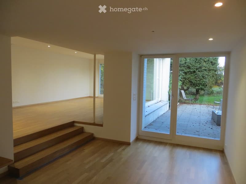Bright, unfurnished room with wooden flooring, large sliding glass doors leading to a patio, and a small staircase leading to another level.