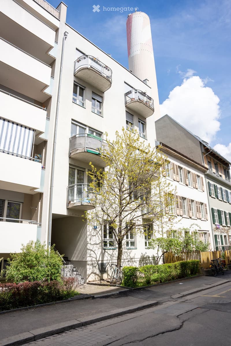 Modern multi-story apartment building with white facade, multiple balconies, and a cylindrical tower on the roof.