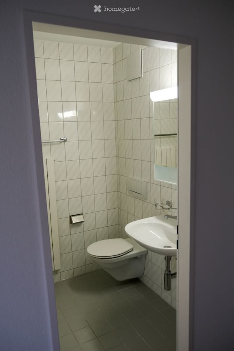 Modern bathroom with white tiled walls, a toilet, a sink with a mirror, and a chrome faucet.