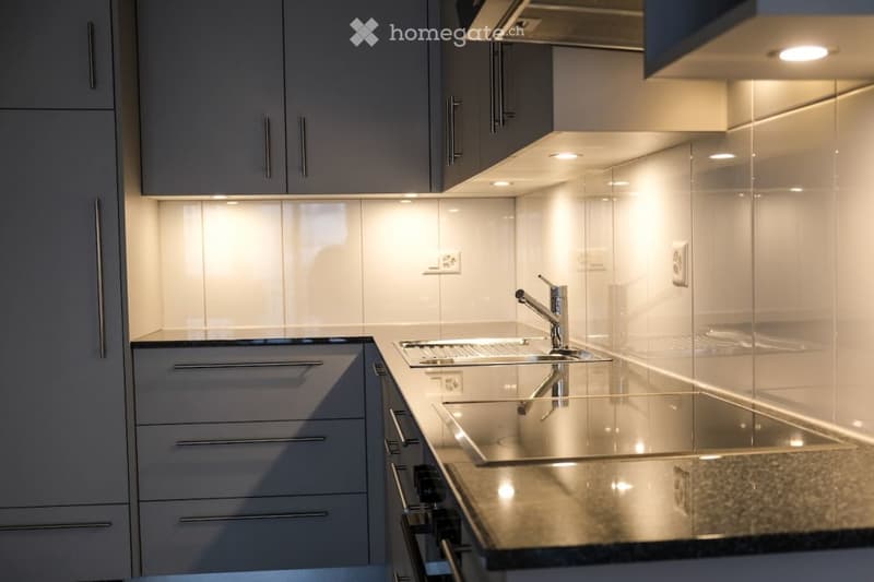 Modern kitchen with sleek grey cabinets, stainless steel sink, and built-in lighting. The countertop is made of a polished stone material, and the space features a minimalist design with integrated storage.