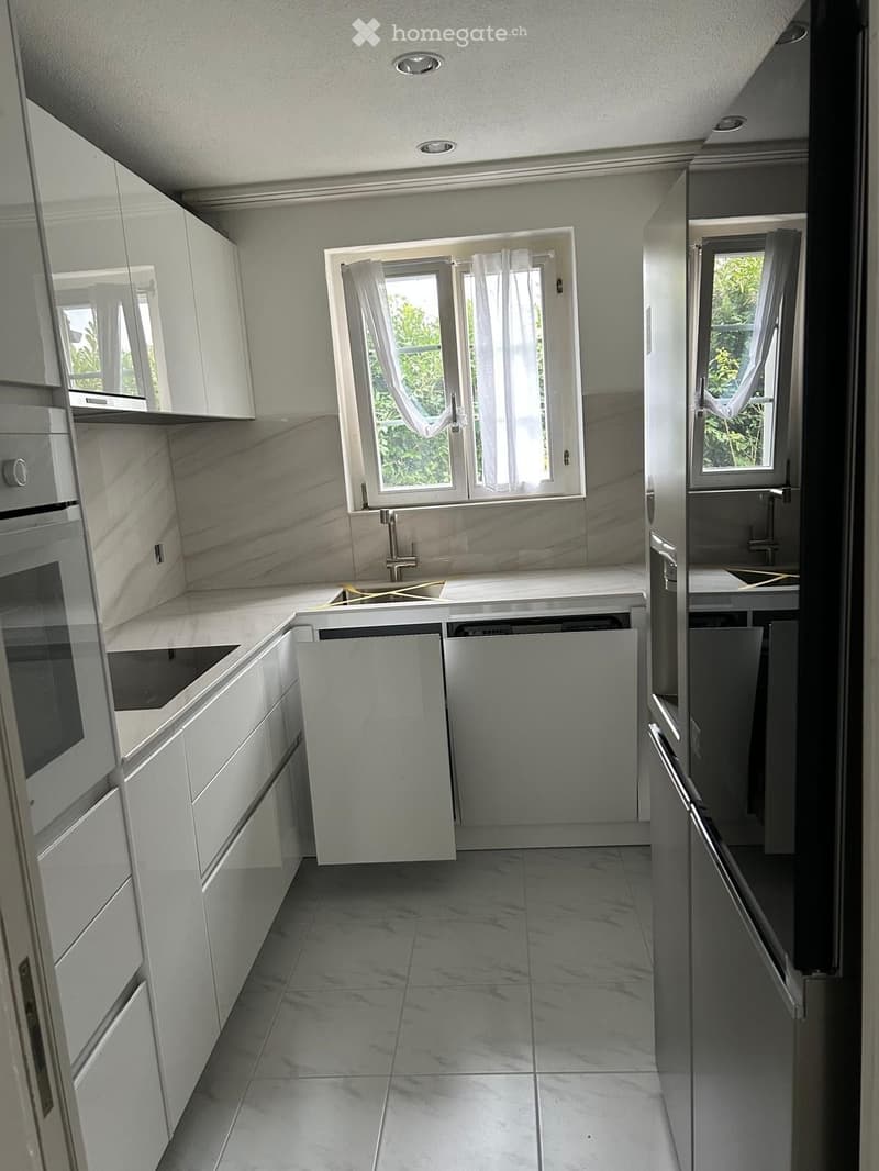 Modern kitchen with white cabinets, marble countertops, and stainless steel appliances. Features a sink, faucet, and built-in oven.