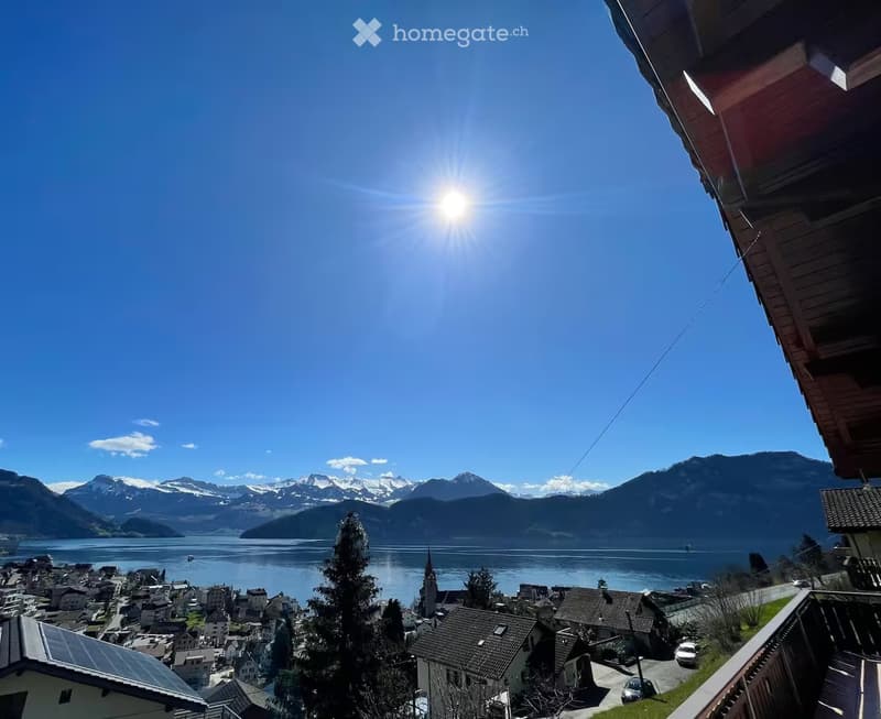 Balcony overlooking a picturesque town with a lake and snow-capped mountains in the background.