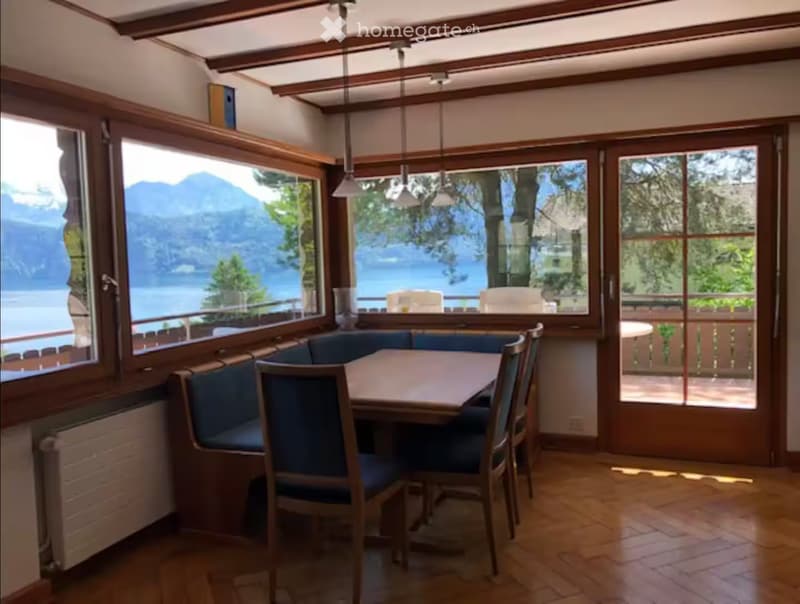 Bright dining area with large windows overlooking a scenic lake and mountains, featuring a wooden table, chairs, and a built-in bench seating.