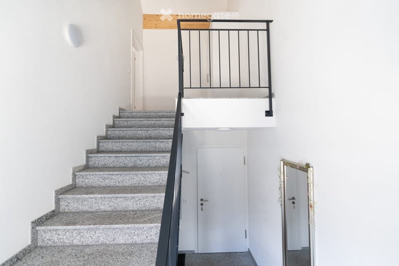 Modern staircase with grey granite steps, black metal railing, white walls, and doors leading to other rooms.