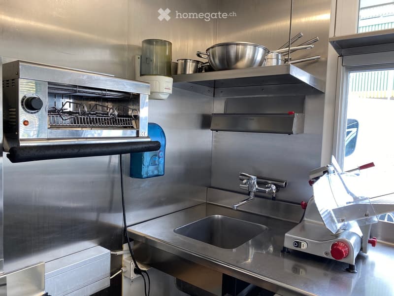 Stainless steel kitchen with oven, fryer, sink, and various pots and pans on shelves.