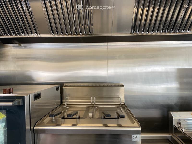 Stainless steel kitchen with a fryer, oven, sink, and a small cup on the counter.