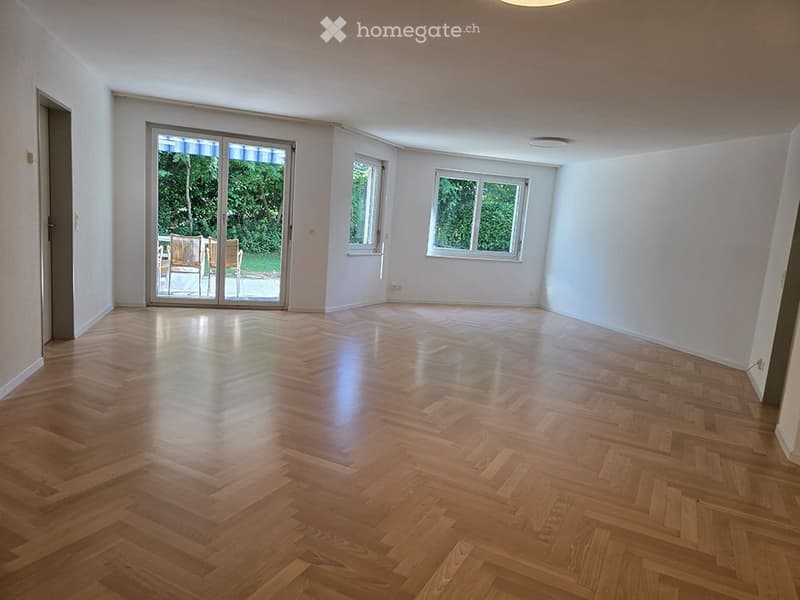 Empty room with wooden flooring, white walls, large windows, and a sliding glass door leading to an outdoor area.