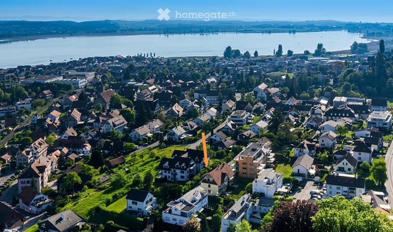 Aerial view of a residential neighborhood with numerous houses, surrounded by greenery and a body of water in the background.