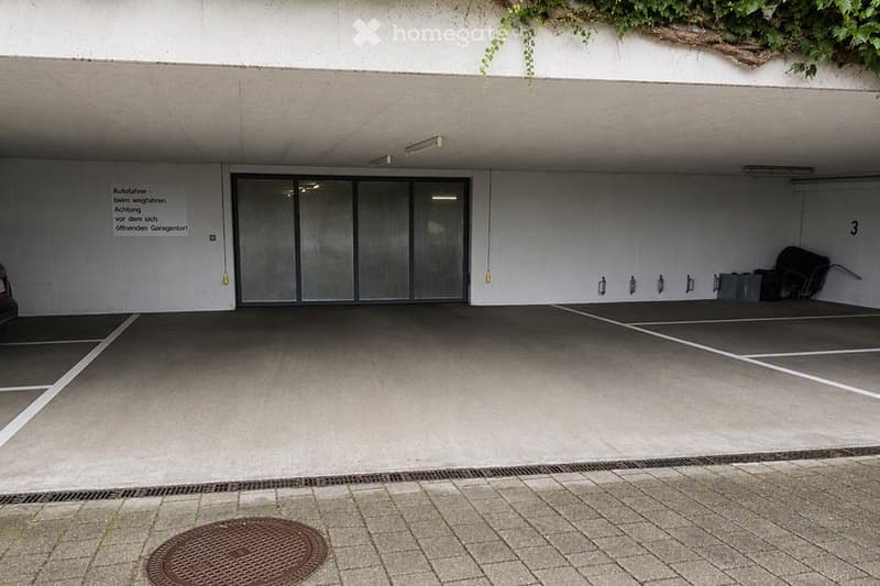 Underground garage with concrete floor, marked parking spaces, and a large automatic door.