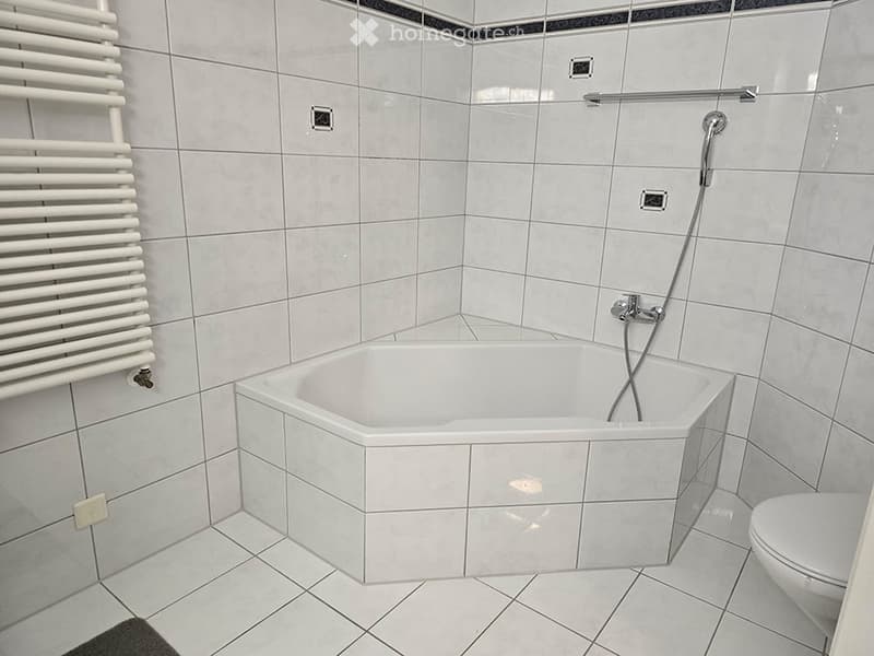 Modern bathroom with a white tiled bathtub, toilet, and a white radiator on the wall.