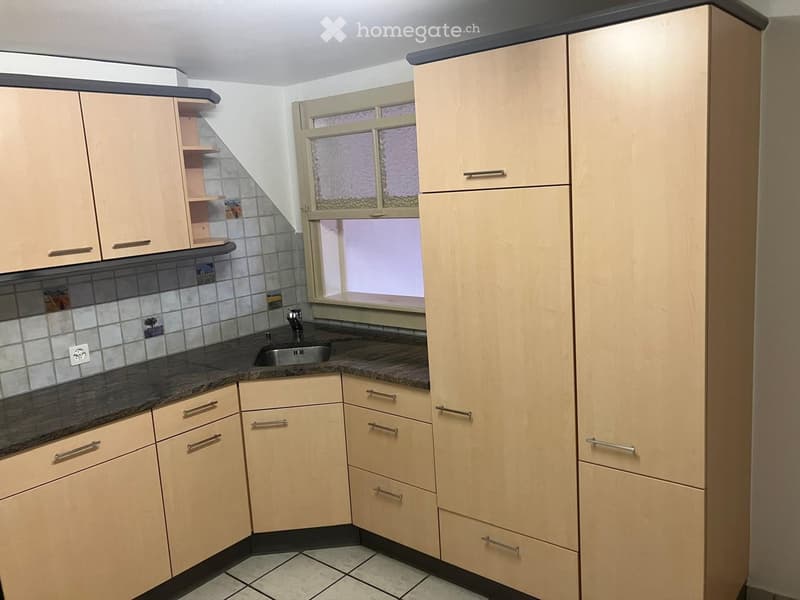 Modern kitchen with light wood cabinets, granite countertop, and a window with frosted glass. The sink is visible with a faucet, and the cabinets have silver handles.