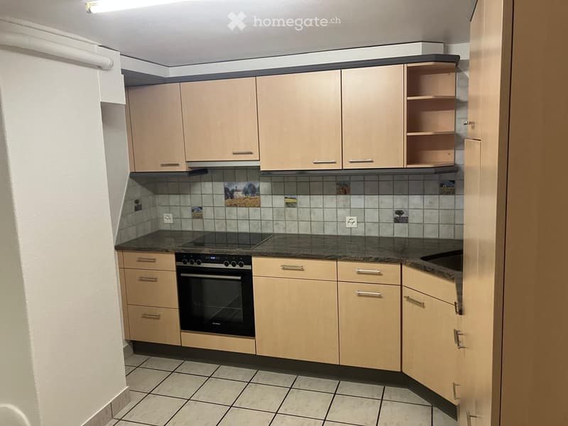 Modern kitchen with light wood cabinets, granite countertop, and built-in oven. Features tiled backsplash with decorative tiles and tiled flooring.
