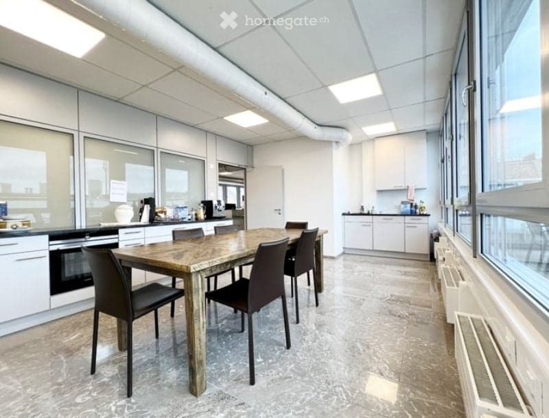 Bright, modern break room with a large wooden dining table and chairs, white kitchen cabinets, and a coffee machine area.