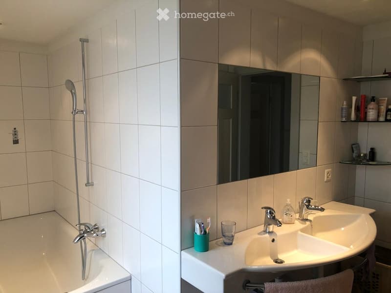 Modern bathroom with a bathtub, shower, double sink, and mirrored cabinet. Includes toiletries, a toothbrush holder, and a cup on the counter.