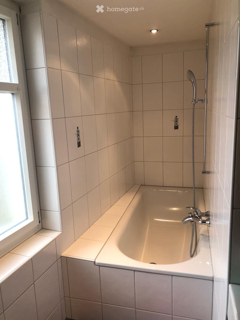 Modern bathroom with a bathtub, tiled walls, and a showerhead attached to the wall.