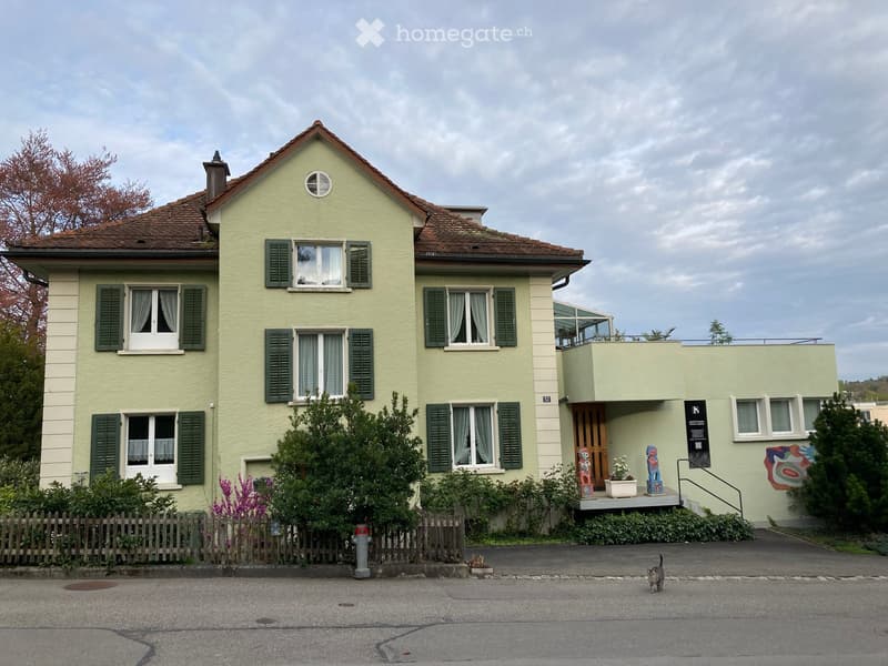 House. Two-story house with light green exterior, multiple windows with green shutters, small balcony, and decorative artwork on the wall.