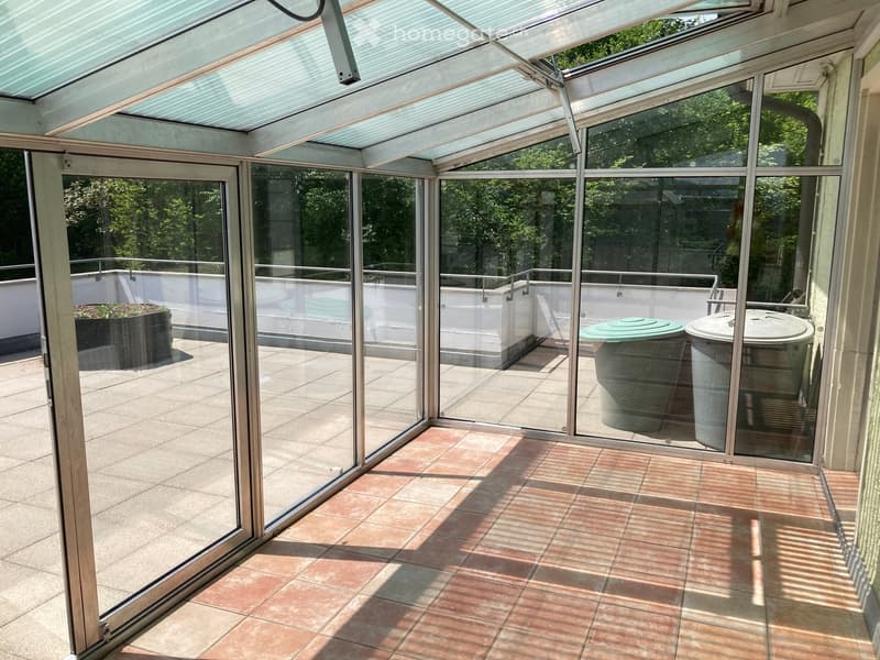 Balcony / Terrace. Glass-enclosed balcony with tiled flooring, large sliding glass doors, and outdoor furniture visible through the glass.