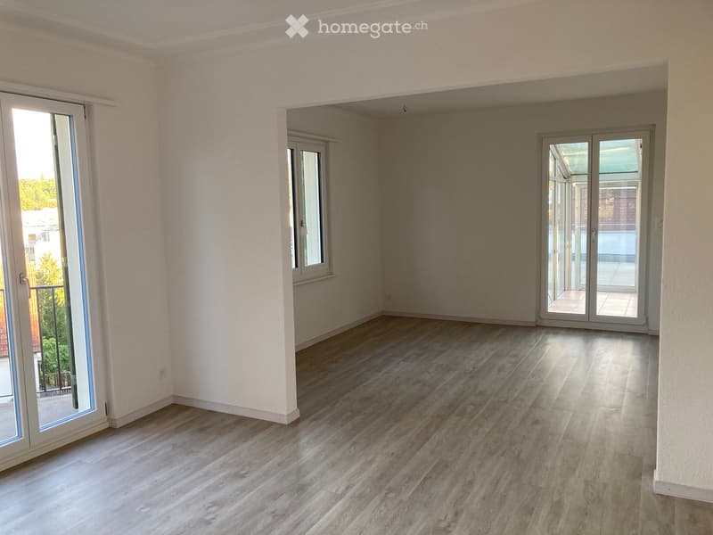 Empty room with light wooden flooring, white walls, and large windows with sliding doors leading to a balcony.