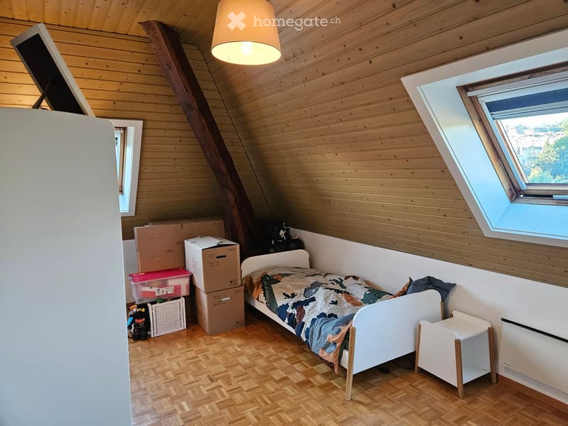 Cozy attic bedroom with wooden walls and slanted ceiling, featuring a single bed with a colorful blanket, a nightstand, storage boxes, and a wicker basket.