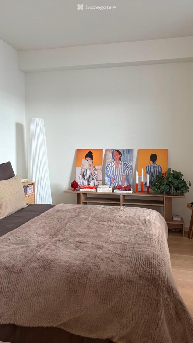 Cozy bedroom with a large bed, nightstand, wooden table with books and candles, and artwork on the wall.