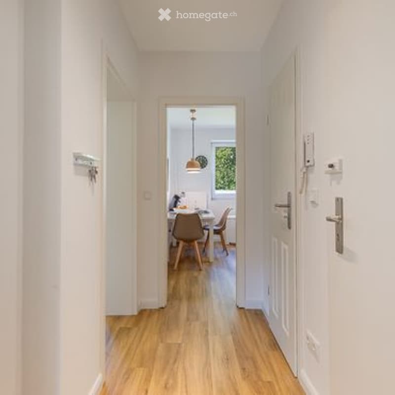 Bright hallway with wooden flooring, leading to a dining area with a round table and chairs.