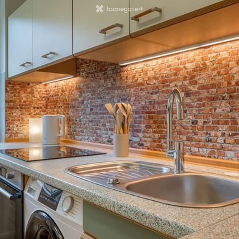 Modern kitchen with a brick backsplash, stainless steel sink, induction stove, and white cabinets.