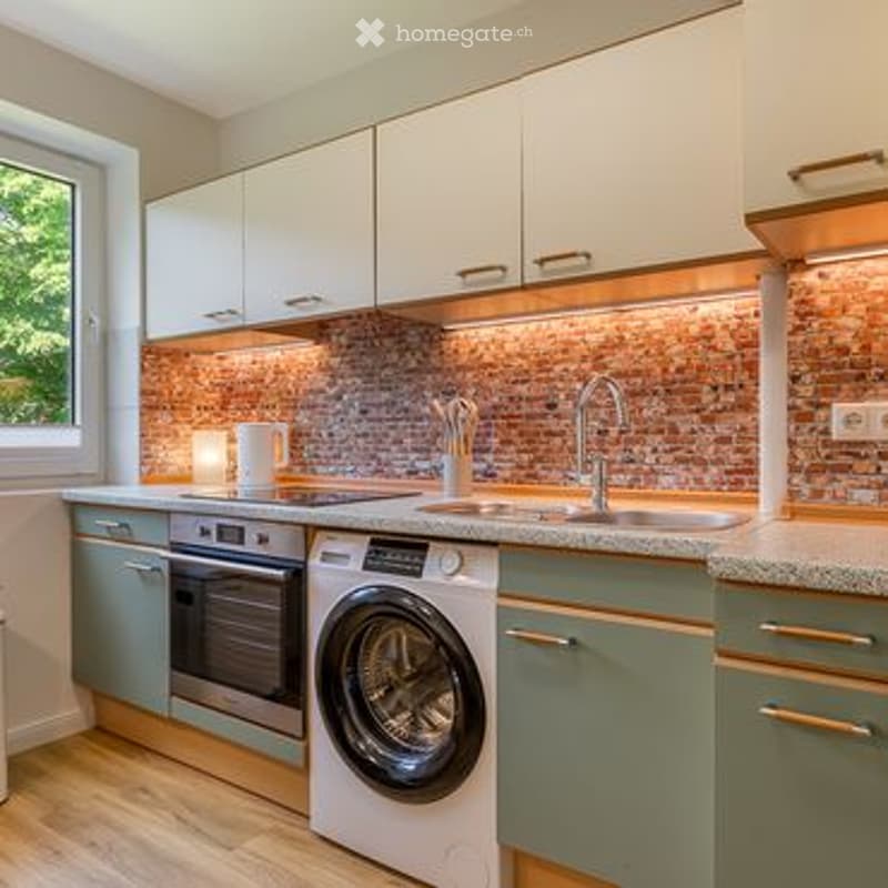 Modern kitchen with white cabinets, a brick backsplash, a sink with a faucet, an oven, and a washing machine.