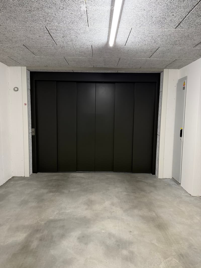 Empty room with concrete floor, white walls, and a black elevator door at the back.