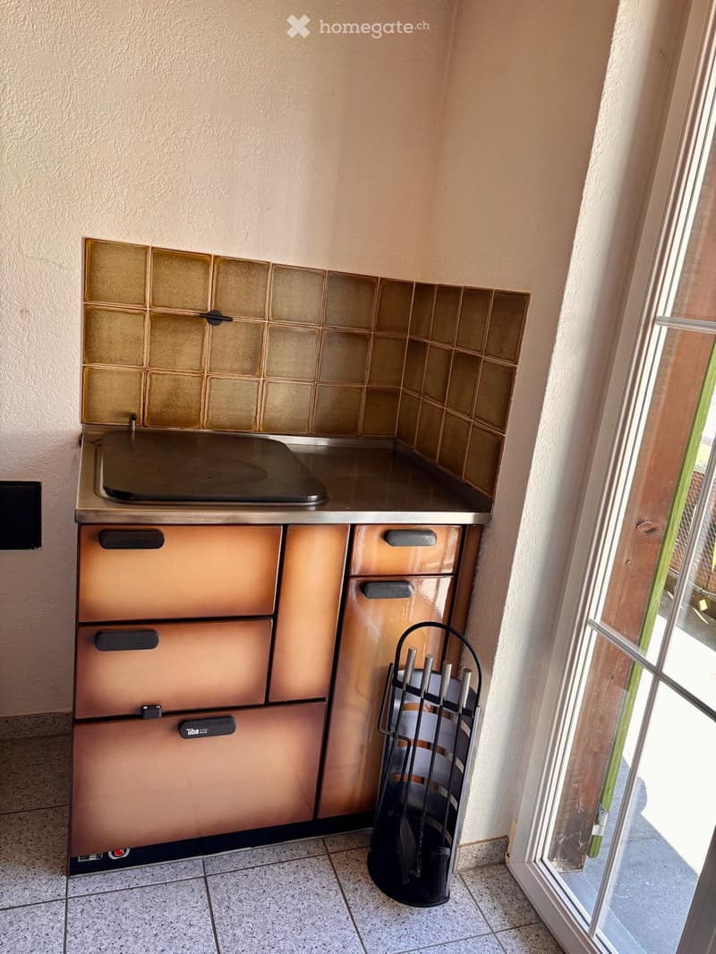 Compact kitchen with a built-in stove, tiled backsplash, and storage cabinets.