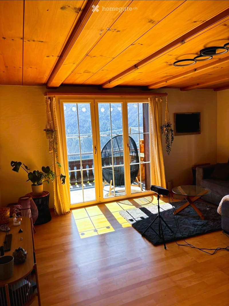 Bright living room with wooden floors, large windows offering a scenic view, a sofa, coffee table, glass table, and potted plants.