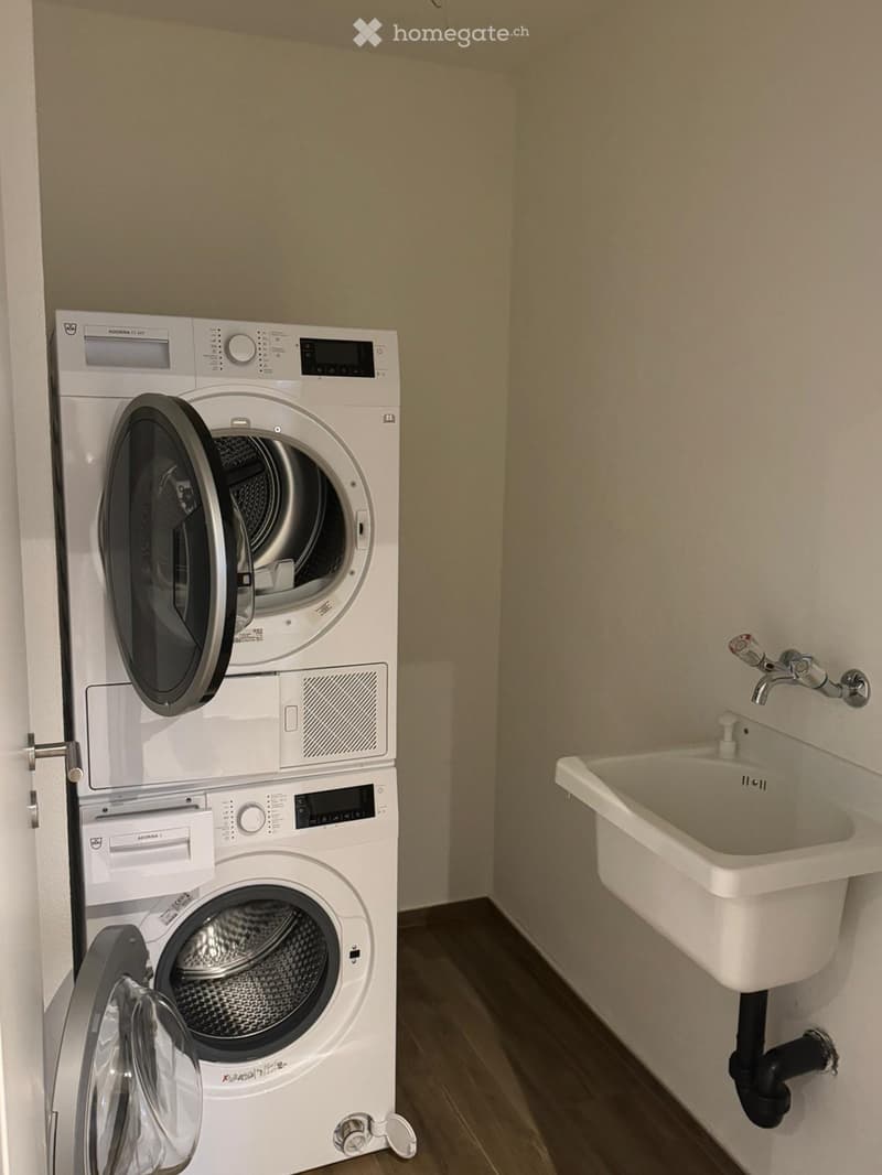 Bathroom with a stacked washing machine and dryer unit, a white sink with a faucet, and beige walls.