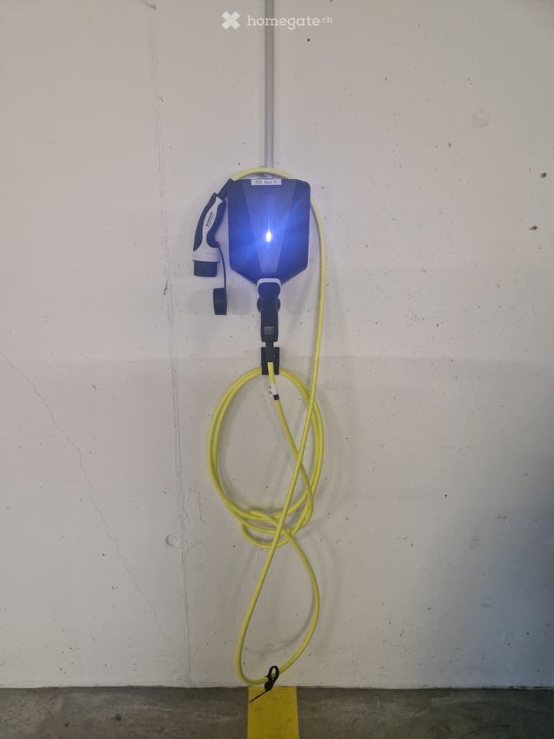 A water hose and nozzle mounted on a white wall, with a yellow coiled hose and a blue nozzle attached.