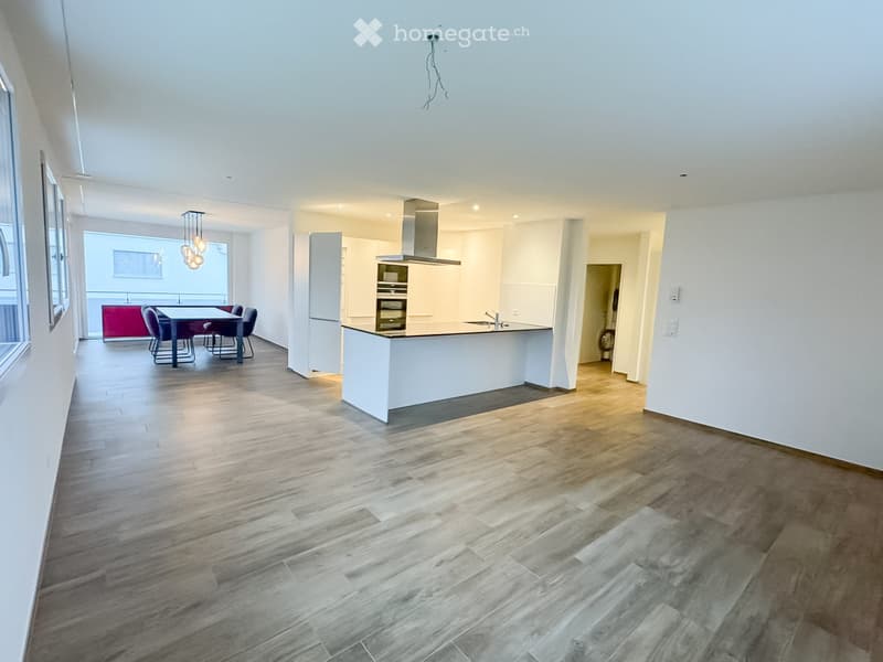 Open-plan living and dining area with modern kitchen, dining table, chairs, and integrated appliances.