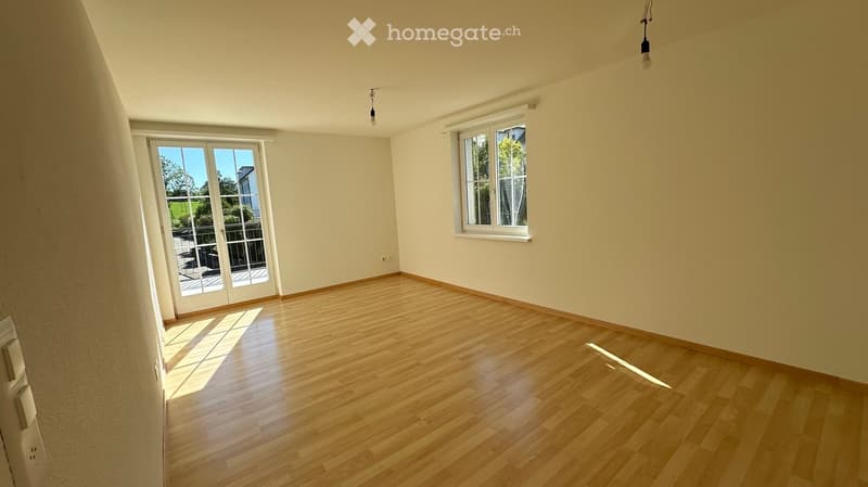 Empty room with wooden flooring, large windows, and a sliding glass door leading to a balcony.