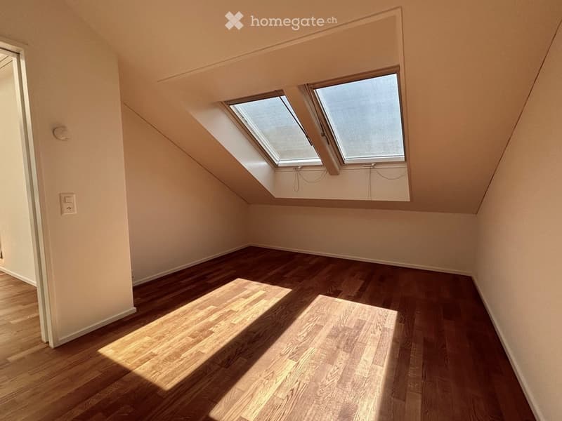 Empty attic room with wooden flooring, slanted ceilings, and two skylight windows allowing natural light to enter.