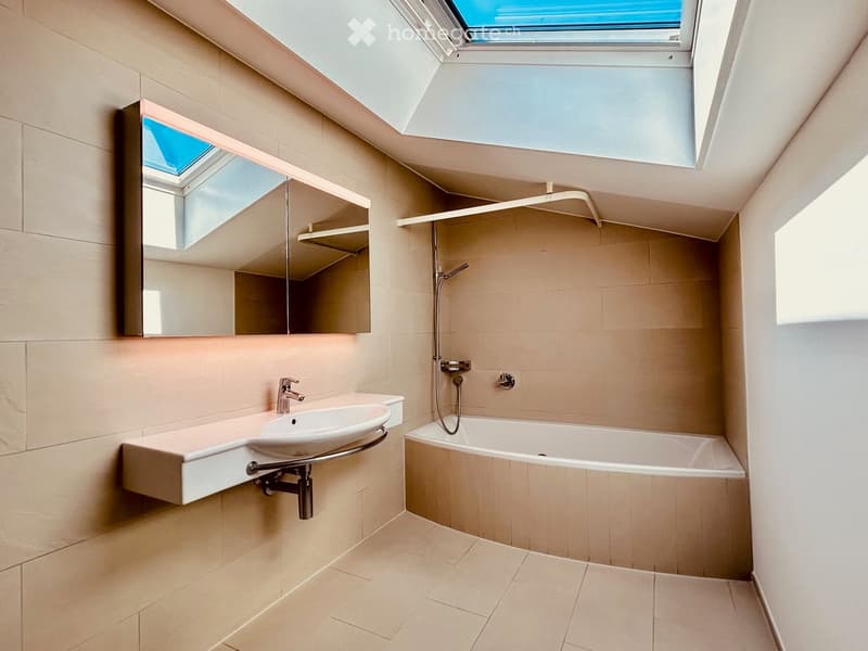 Modern bathroom with a bathtub, sink, and large mirror. Features a skylight window and sleek, contemporary design.