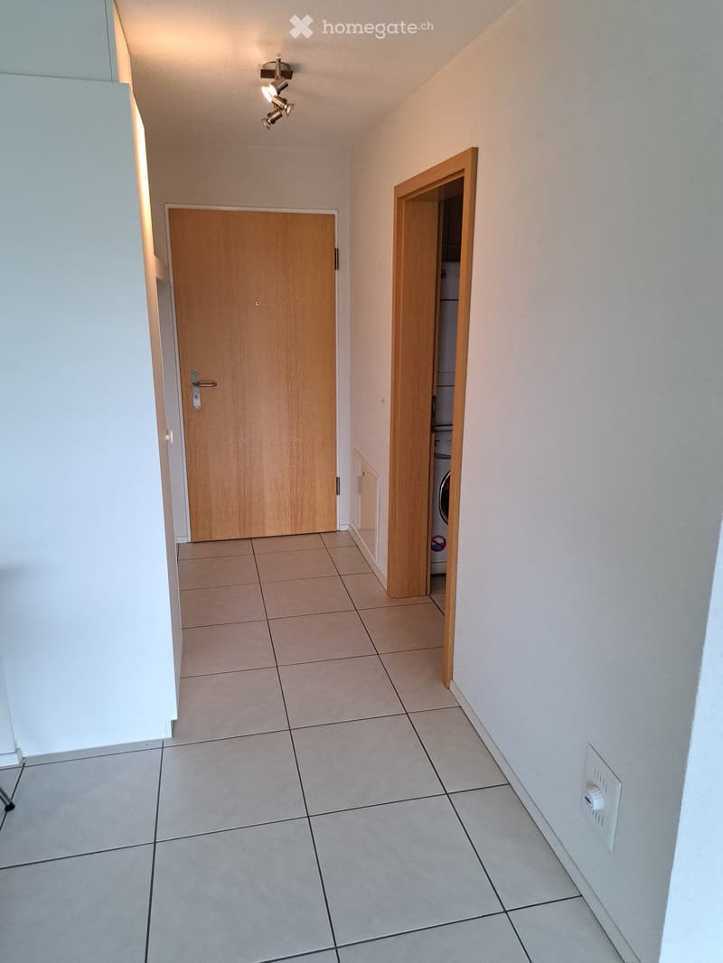 Empty hallway with tiled floor, two wooden doors, and a small open closet containing a washing machine.