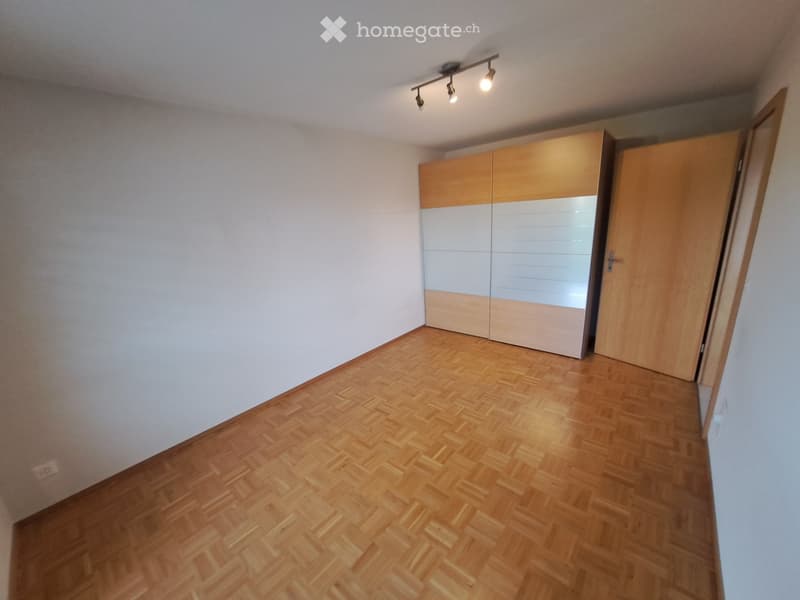 Empty room with light wooden flooring, white walls, and a built-in wardrobe with mirrored doors.